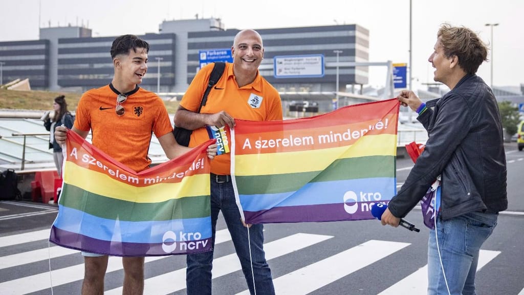 Apresentador holandês Klaas van Kruistum com a bandeira do arco-íris, no aeroporto de Amesterdão, antes do Países Baixos-República Checa (Ramon Van Flymen/AP)

