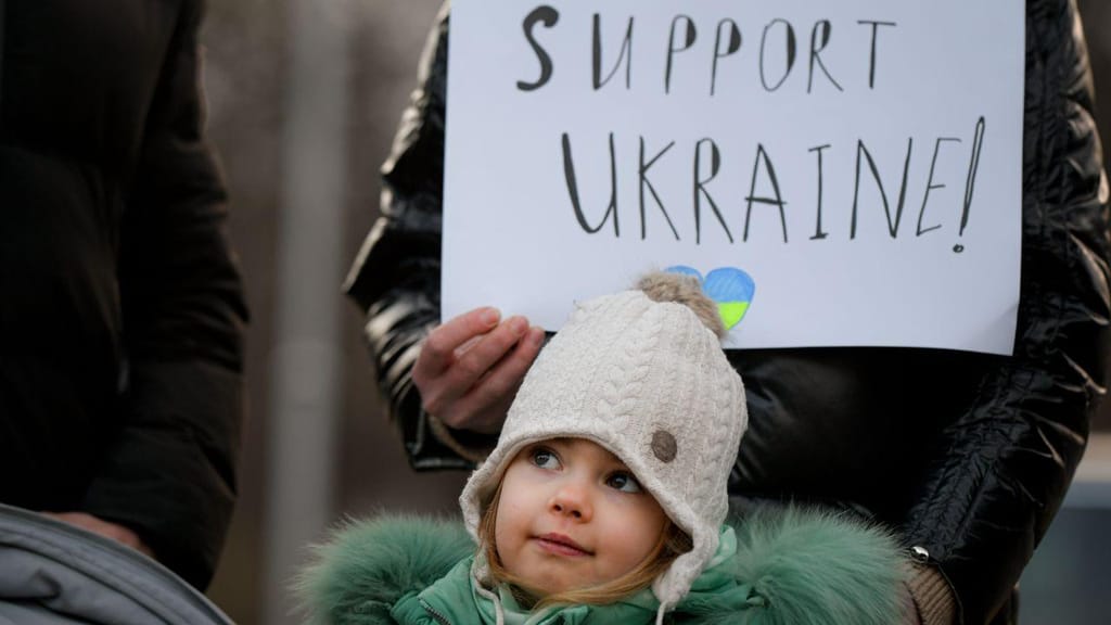 Criança brinca com uma bandeira da Ucrânia durante protesto em frente à embaixada ucraniana em Bucareste, Roménia (AP Photo/Andreea Alexandru)