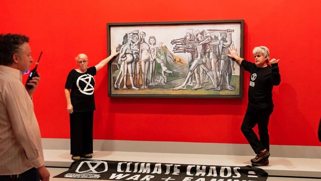 Ativistas colam-se à cobertura de vidro da obra de Picasso “Massacre na Coreia”, ao lado de uma faixa onde se lê “Caos Climático = Guerra e Fome”