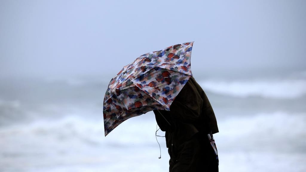 Uma mulher tenta proteger-se da chuva e do vento na marginal da Foz do Douro no Porto, 17 de outubro de 2023 (ESTELA SILVA/Lusa)