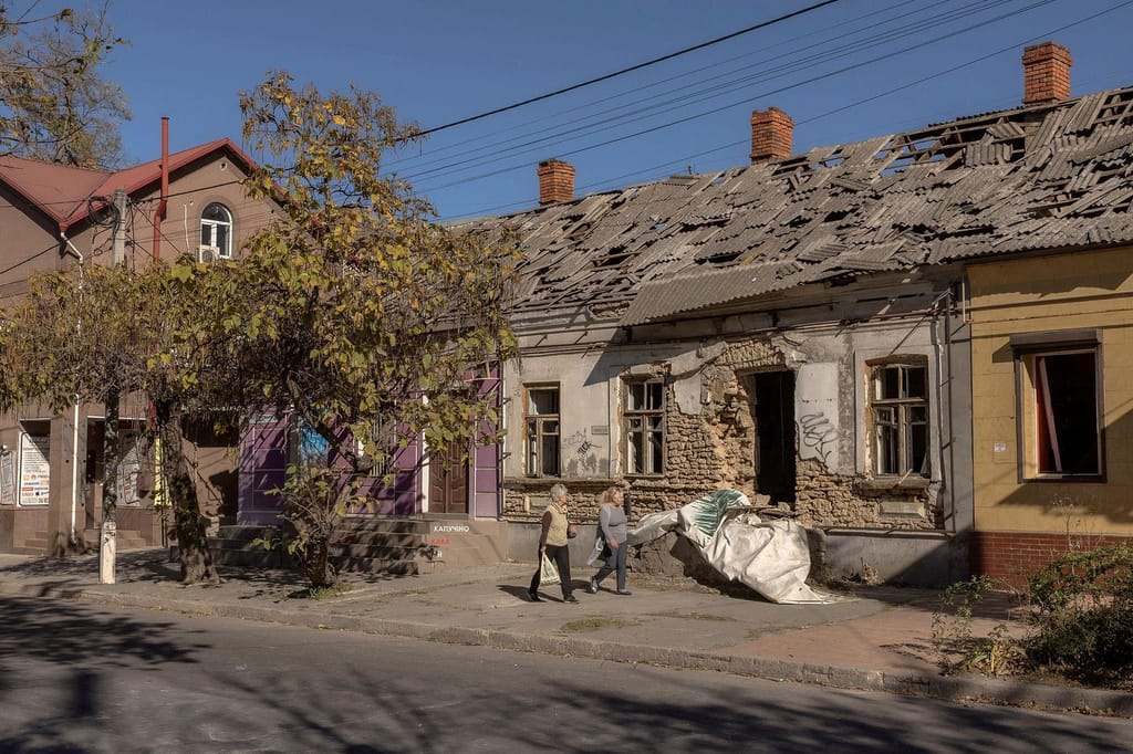 Pessoas passam por um edifício danificado num recente ataque russo na cidade de Kherson, no sul da Ucrânia, a 29 de outubro de 2023. Roman Pilipey/AFP/Getty Images