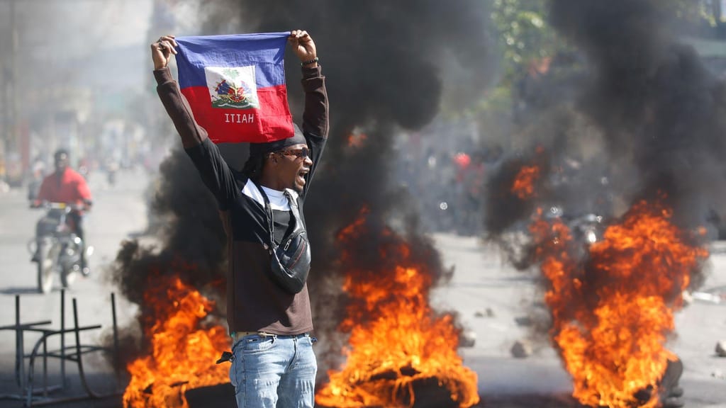 Manifestante com bandeira do Haiti no meio do caos de Port-au-Prince (Odelyn Joseph/AP)