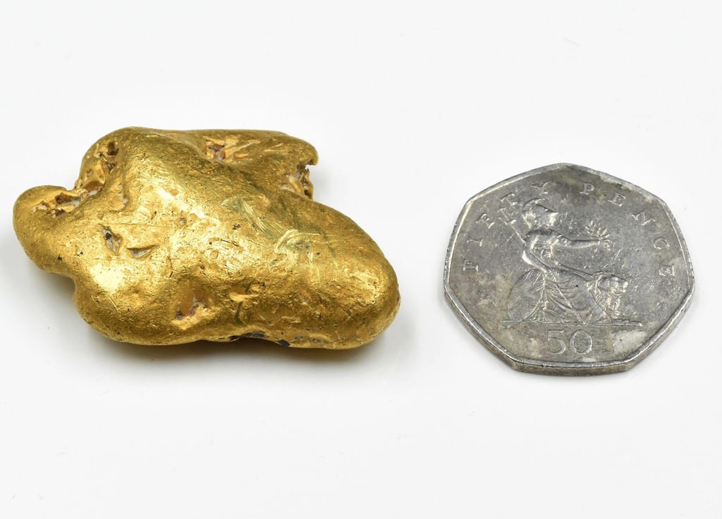 A pepita de ouro, mostrada ao lado de uma moeda de 50 pence do Reino Unido [maior que a moeda de dois euros]. Cortesia de Mullock Jones